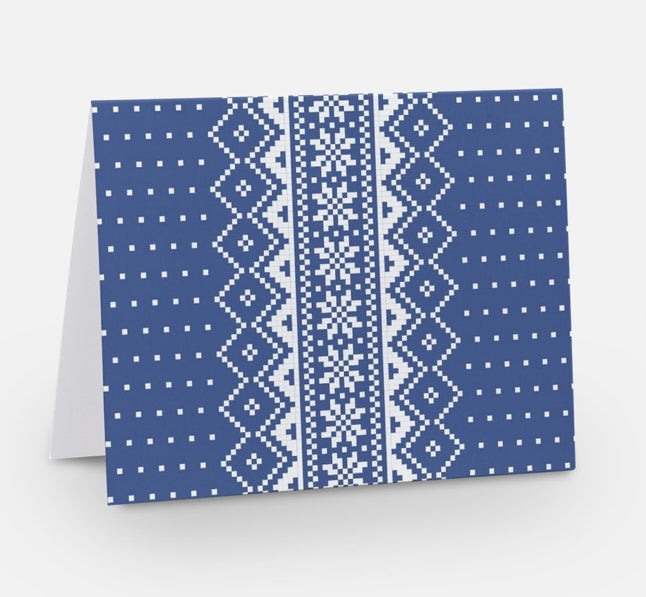 A blue notecard with a traditional Nordic pattern consisting of white floral and geometric designs from The Uff Da Sisters.