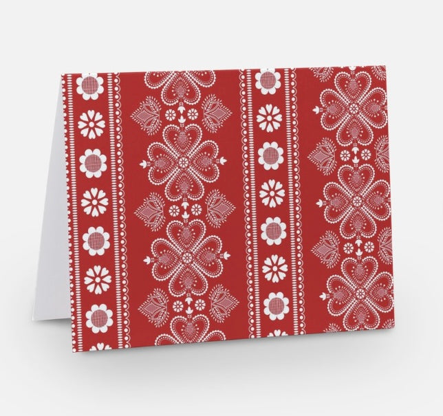 A red notecard with a traditional Nordic pattern consisting of white floral and geometric designs from The Uff Da Sisters.