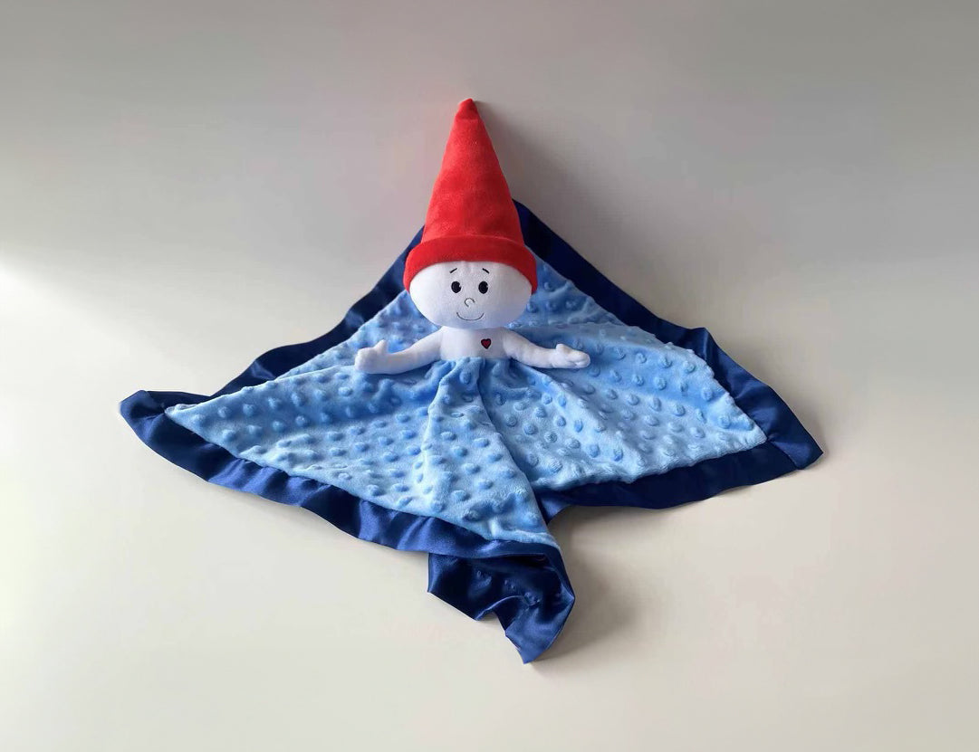 The Gnome Lovey is a stuffed doll attached to a light blue blanket with navy blue trim. The lovey's face and body is white, with a tall red gnome hat and a small red heart embroidered on the left side of it's chest.