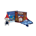 The children's book "Gnome Needs A Home" is displayed open alongside a plush gnome doll and a comforting gnome lovey blanket. The doll and lovey both feature a gnome character with a red hat, mirroring the book's charming theme. The book's cover shows a worried gnome character and the interior pages offer engaging text and colorful illustrations.