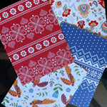 A collection of four notecards with Nordic designs from The Uff Da Sisters, featuring patterns in red with white floral motifs, grey with multicolored flowers, white with colorful birds and floral designs, and blue with white geometric patterns.