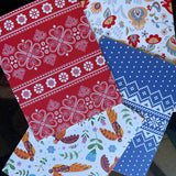 A collection of four notecards with Nordic designs from The Uff Da Sisters, featuring patterns in red with white floral motifs, grey with multicolored flowers, white with colorful birds and floral designs, and blue with white geometric patterns.